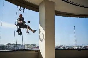 Travailleur Cordiste isolé suspendu en hauteur réalisant des travaux en extérieur sur façade vitrée dans un contexte de travail isolé